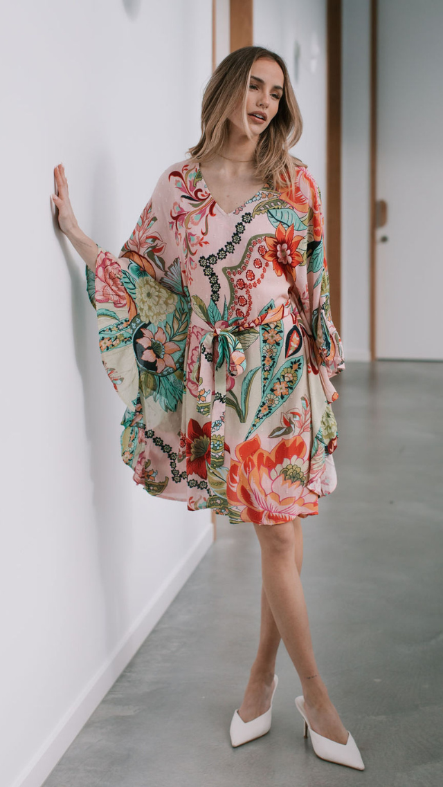 Woman wearing the Moorea Dress, a short floral kimono-style dress with wide sleeves, waist tie, and vibrant tropical print.