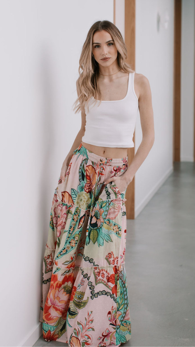 Woman wearing the Palmier Skirt in bold floral print with tiered maxi silhouette and elastic waistband, styled with a white tank top.