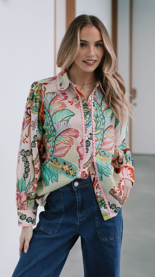 Woman wearing the Tropenza Shirt in tropical floral print with pink pom-pom trim, styled with dark blue denim jeans.