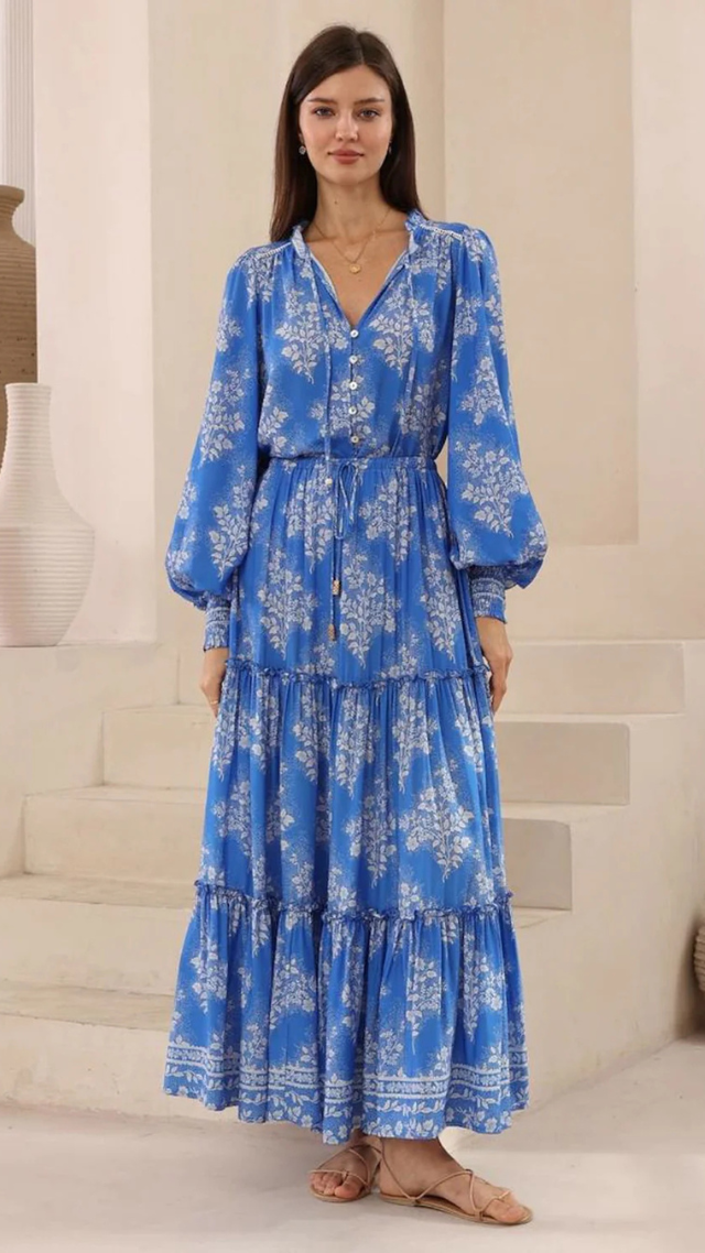 Model wearing the Boulevard Skirt in blue with white floral print, featuring a tiered maxi silhouette, drawstring waistband, and tassel details.