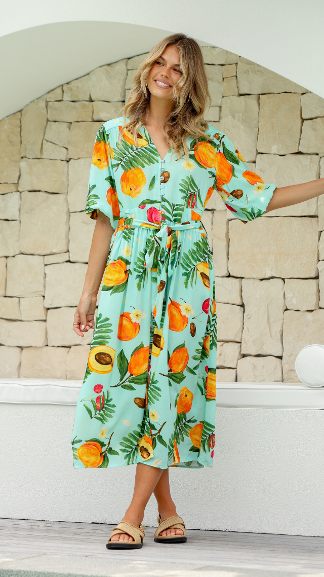 Model wearing the Italia Midi Dress – aqua button-down dress with papaya fruit print, midi length, tie waist, and short sleeves.
